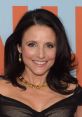 Julia Louis-Dreyfus smiles warmly, showcasing her elegant look with a black outfit and golden jewelry at a red carpet event.