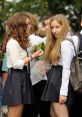 Russian girls in school outfits holding flowers, celebrating a special occasion with friends outdoors.