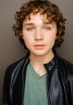 Portrait of young male with curly hair and green eyes, wearing a black jacket and green shirt, showcasing youthful charm.