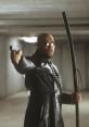 Morpheus, portrayed by Laurence Fishburne, aiming a gun with a stick in a dimly lit setting, embodying strength and resolve.