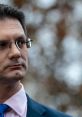 Steve Baker in a formal suit, thoughtfully gazing with an intense expression, set against a blurred natural background.