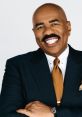 Steve Harvey smiling confidently in a tailored suit with an orange tie, showcasing his signature style and charismatic persona.