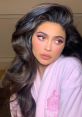 Kylie Jenner flaunts glamorous makeup and wavy hair, wearing a cozy pink robe in a chic, indoor setting.