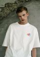 Young model wearing a stylish white oversized t-shirt with colorful graphic design against a textured wall backdrop.