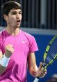 Carlos Alcaraz celebrating a victory on the tennis court, wearing a pink shirt and holding his racquet with enthusiasm.