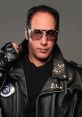 Andrew Dice Clay in a leather jacket with studs, wearing sunglasses, embodying his iconic comedian persona.