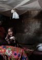 A mother holding her playful daughter in a dimly lit room, showcasing intimacy and care in a modest setting.