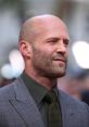 Jason Statham sports a stylish grey suit and green tie, exuding confidence at a red carpet event.