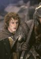 Frodo Baggins looks concerned while holding a weapon beside a heavily armored warrior in "The Lord of the Rings.