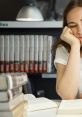 Student looking bored while studying in a library, surrounded by books and a lamp, conveying a sense of distraction.