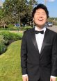 Disguised Toast in a tuxedo, smiling outdoors amidst greenery, showcasing a cheerful and stylish look.