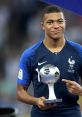 Kylian Mbappé proudly holding his trophy, celebrating his achievements in international football.