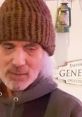 Doug Campbell wearing a brown beanie in front of a grocery store sign, capturing a casual moment in a rustic setting.