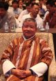 Kelzang Dorji seated at a conference, wearing traditional Bhutanese attire, engaged with an audience in the background.