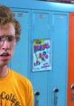 Napoleon Dynamite in college tee stands by colorful lockers, showcasing his iconic awkwardness and style.