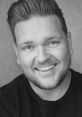 Smiling portrait of Joshua Lloyd, showcasing his charismatic personality and professional charm in a stylish black sweater.