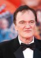 Quentin Tarantino at a film event, showcasing his iconic style and charisma in a tuxedo, with a vibrant background.