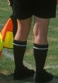 Referee with black socks and skirt, standing on a grassy field, ready to officiate a soccer game, focused and alert.