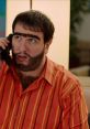 Recep İvedik character on phone, sporting a vibrant striped shirt and distinct facial hair, showcasing Şahan Gökbakar's humor.