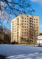 Snow-covered playground beside a residential building, featuring yellow swings and leafless trees against a blue sky.