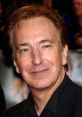 Alan Rickman smiling at a film premiere, showcasing his distinctive hairstyle and charismatic presence.