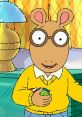 Arthur Read smiles while holding a toy, wearing a yellow sweater and glasses in a cozy home setting.