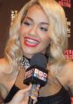 Rita Ora smiles brightly while being interviewed, showcasing her glamorous style at a music event.