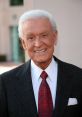 Bob Barker smiles in a formal suit with a red patterned tie, showcasing his iconic television persona.