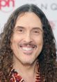 Weird Al Yankovic smiles at a red carpet event, showcasing his signature curly hair and vibrant personality.