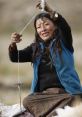 Tibetan woman skillfully spinning yarn with a drop spindle, showcasing traditional textile crafting techniques in natural setting.