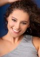 Smiling woman with curly hair wearing hoop earrings and a gray top, showcasing vibrant personality and charm.