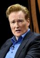 Conan O'Brien speaking during an event, showcasing his signature hair and expressive facial demeanor.