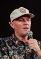 Fred Durst speaking at an event, wearing a floral shirt and cap, holding a microphone, sharing insights on his music career.