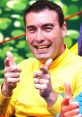 Greg Page smiles and points playfully while wearing a bright yellow shirt, embodying fun and joy for children's entertainment.