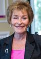 Judge Judy smiling confidently in a stylish black blazer over a pink top, embodying her iconic television persona.