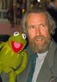 Jim Henson joyfully poses with Kermit the Frog, showcasing the iconic puppet's signature bright green color and playful smile.