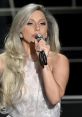 Lady Gaga passionately singing into a microphone, showcasing her stunning fashion and signature long hair.