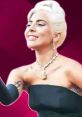 Lady Gaga smiling and talking, showcasing her elegant style with a chic black dress and striking jewelry.