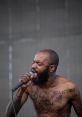 MC Ride passionately performing on stage, showcasing intense energy and striking tattoos during a live concert.