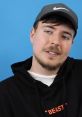 MrBeast in a black hoodie with "BEAST" text, wearing a cap, smiling against a blue background. Popular YouTuber.