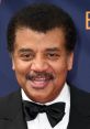 Neil deGrasse Tyson smiling at a red carpet event in a tuxedo with a bow tie, showcasing his charismatic personality.