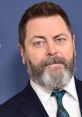 Nick Offerman poses with a serious expression, showcasing his well-groomed beard and stylish attire against a blue backdrop.