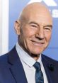 Patrick Stewart, smiling in a navy suit and tie, at a promotional event highlighting his iconic acting career.