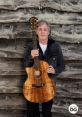 Paul McCartney holding an acoustic guitar, standing against a rustic wooden backdrop, showcasing his musical artistry.