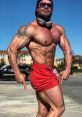 Renato Cariani showcasing impressive physique and muscular definition in athletic red shorts under a blue sky.