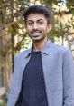 Smiling young man in a stylish gray jacket outdoors, exuding confidence and warmth. Perfect for showcasing Mann Patel's charisma.