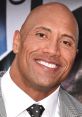 Smiling Dwayne Johnson in a stylish gray suit with a polka dot tie, showcasing charisma and charm at a film event.