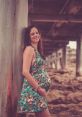 Pregnant woman in a colorful dress smiling, posing gracefully under a pier on a sandy beach, celebrating motherhood.