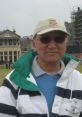 Chang Kuldee enjoying a day outdoors at a golf course, wearing a sporty jacket and cap, with historic buildings in the background.