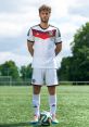 Soccer player stands confidently in Germany's official jersey, ready for action on the field with a colorful ball.